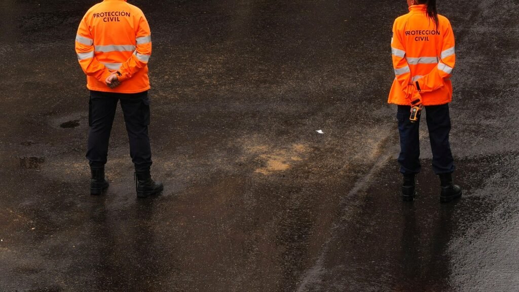 Two civil protection workers in orange hi vis jackets standing on wet pavement