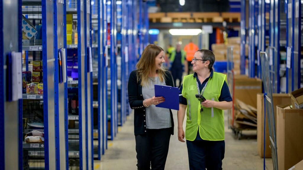 Two women in a warehouse, one wearing a hi vis vest